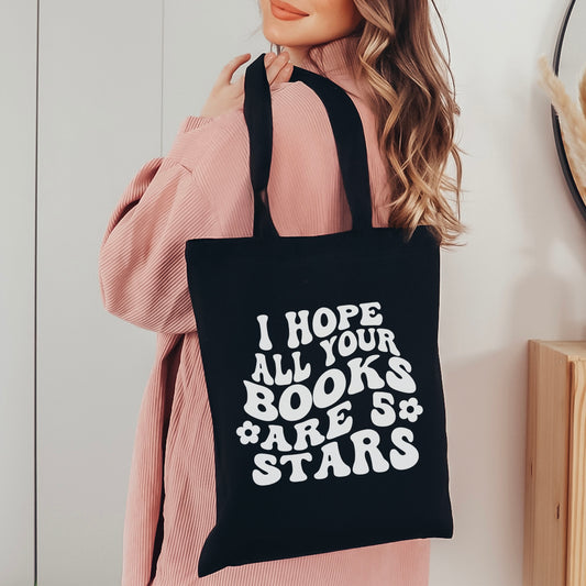 A black canvas tote bag featuring a bold, retro-style design that reads "I Hope All Your Books Are 5 Stars." Carried by a stylish reader in a cozy pink sweater, this bookish tote is perfect for book lovers to carry their favorite reads, bookstore hauls, or everyday essentials in a chic and literary-inspired way.